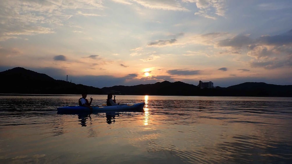 Two people in a blue inflatable raft on calm water with a sunset in the background. 1