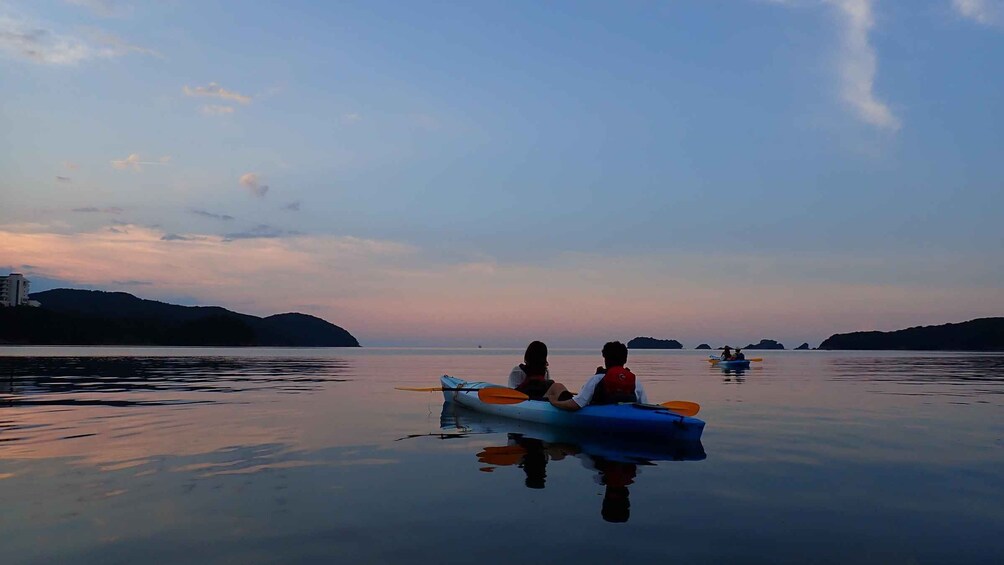 A calm lake with kayaks and people paddling, surrounded by hills and a clear sky. 4