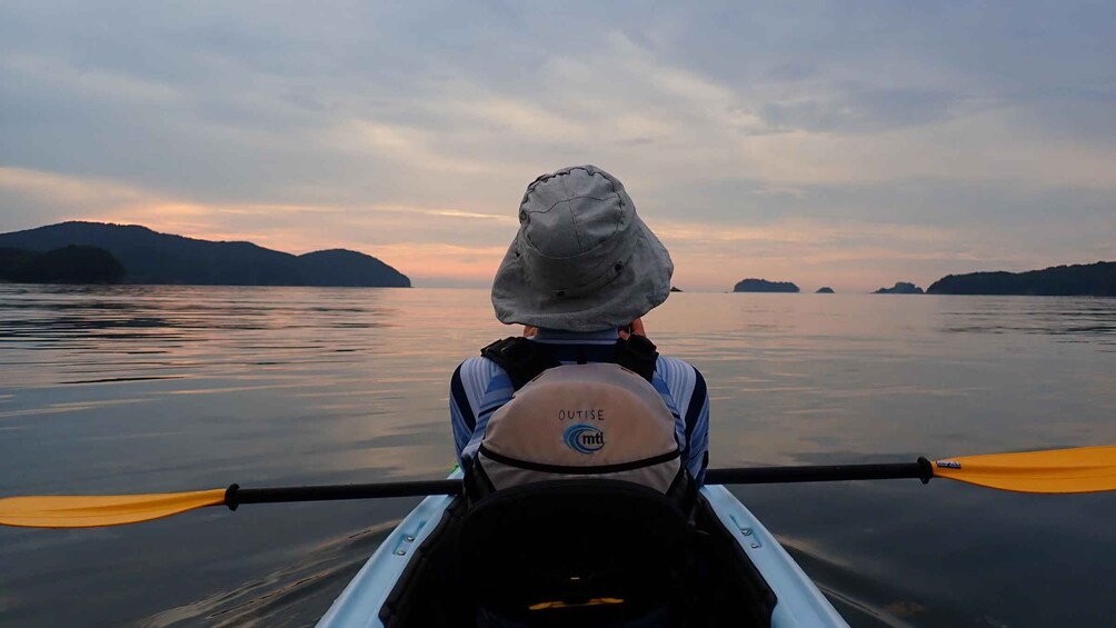 A person in a kayak with a helmet, paddling on calm water with mountains in the background. 2