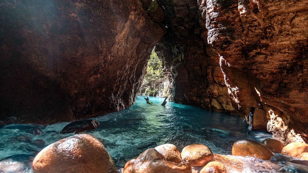 A clear water stream in a rocky cave with large boulders at the bottom. 4