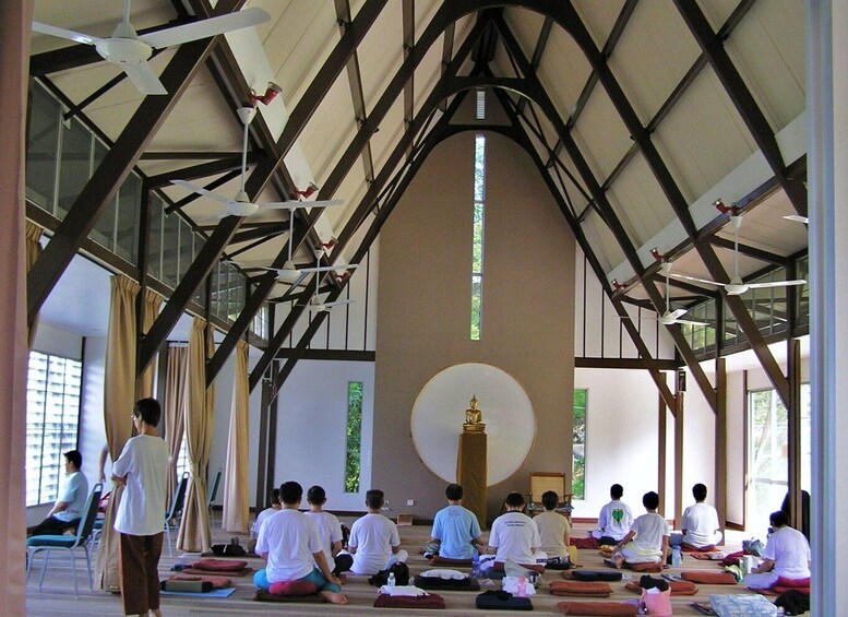 A group of people sitting on mats in a room with a high ceiling and wooden beams. 1
