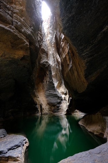 A narrow canyon with a reflective green pool at its base. 5