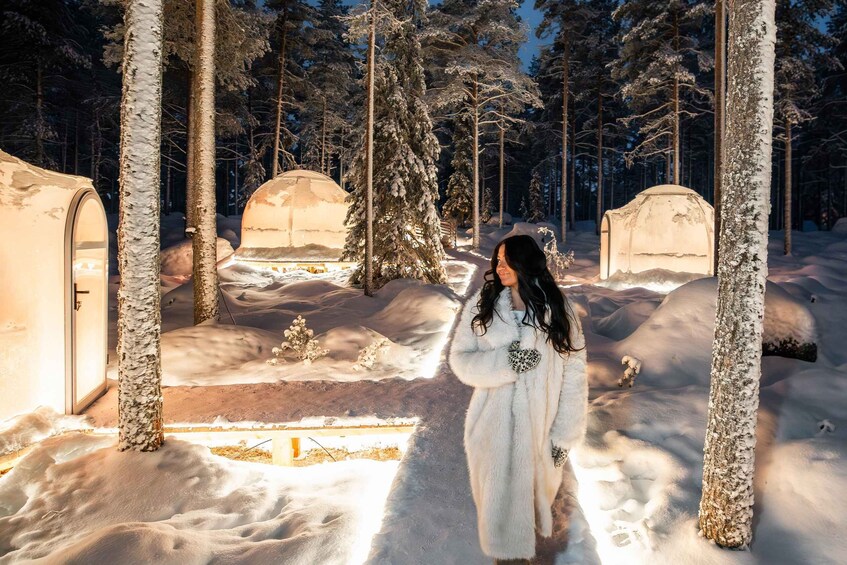 A snowy forest with two illuminated yurts and a person in a white coat. 3