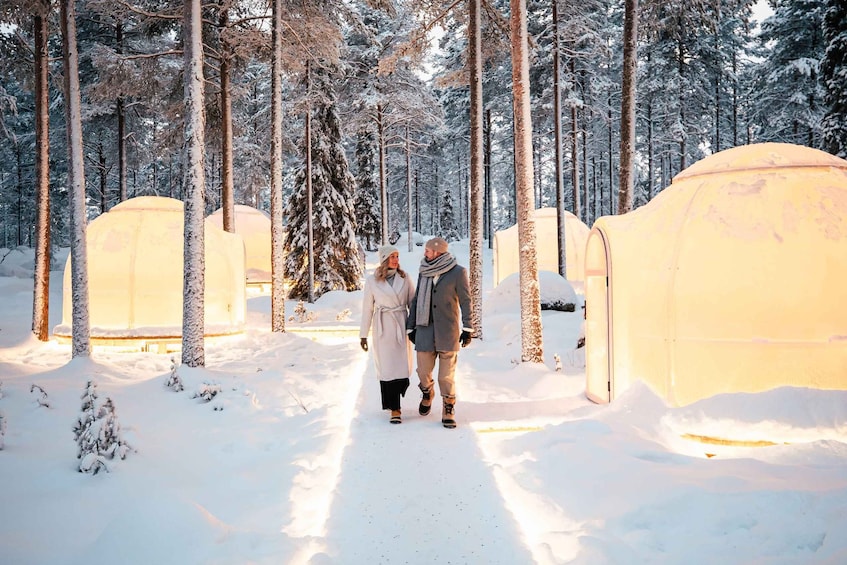 A snowy forest with yurts and a couple walking. 5