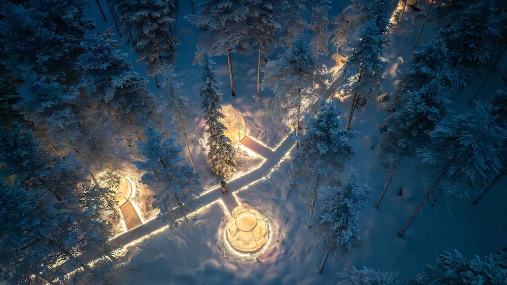 An aerial view of a snow-covered forest with illuminated pathways and a central circular structure. 2