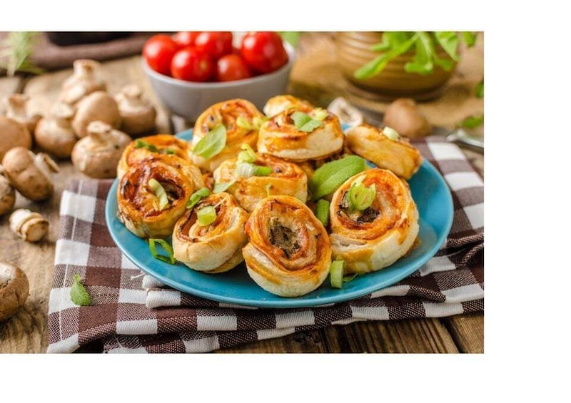 A plate of mushroom rolls garnished with green herbs, with a bowl of cherry tomatoes and mushrooms in the background. 1