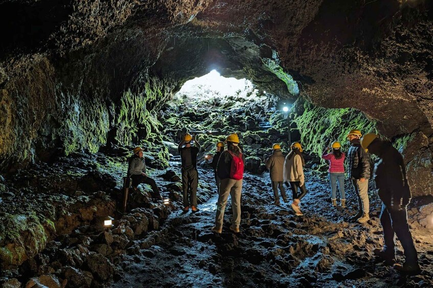 A group of people exploring a cave with green moss and a bright light at the end. 1