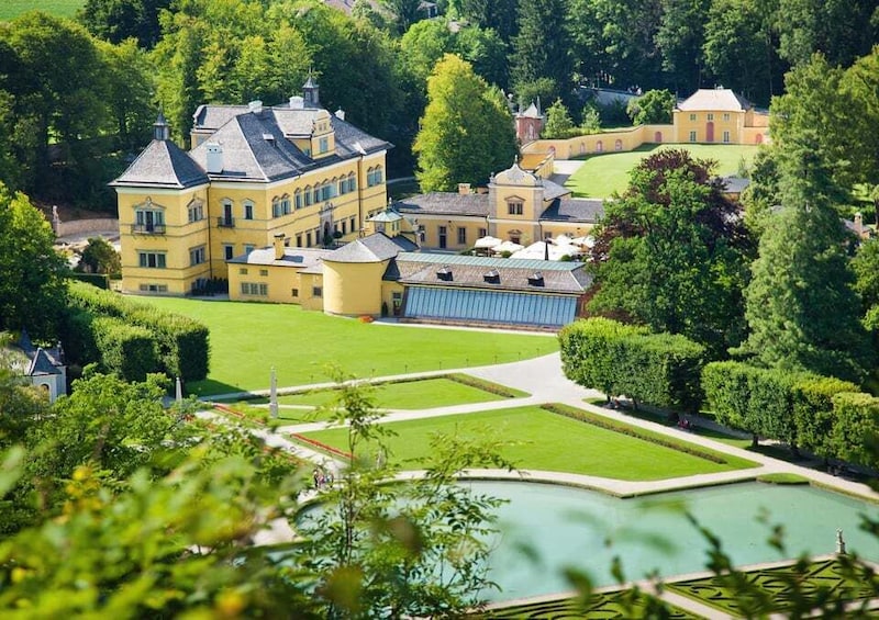 A large yellow building with a garden and a pond. 1