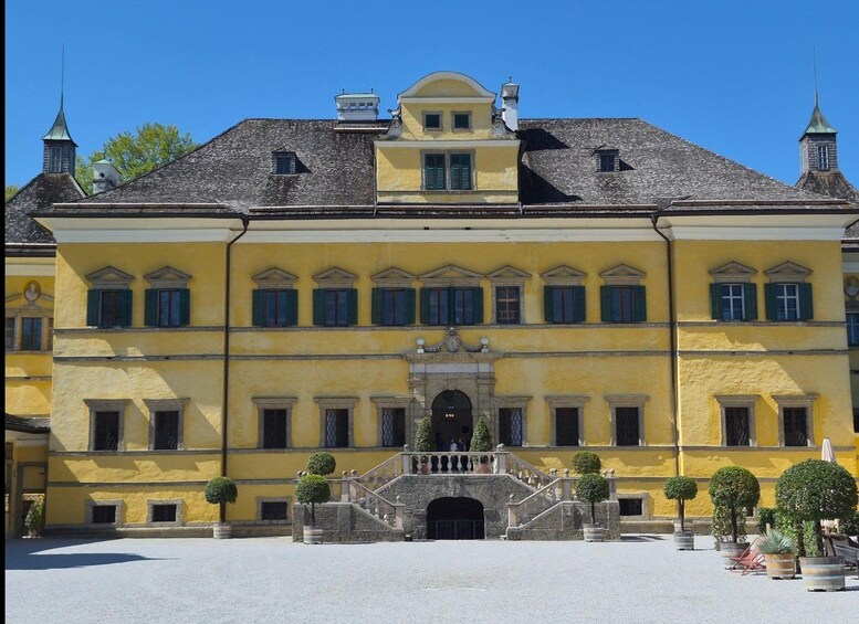 A large yellow building with a central entrance, multiple windows, and a staircase leading to the entrance. 2