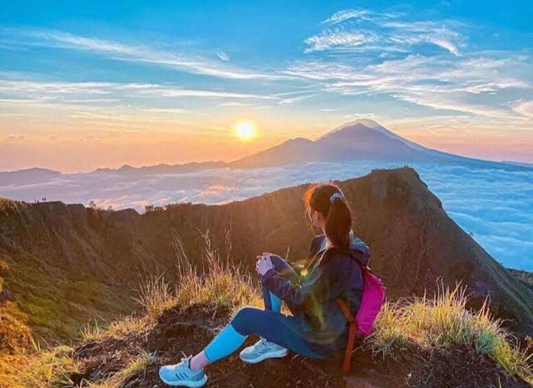 A person sitting on a cliff overlooking a mountain range with a sunset in the background. 2