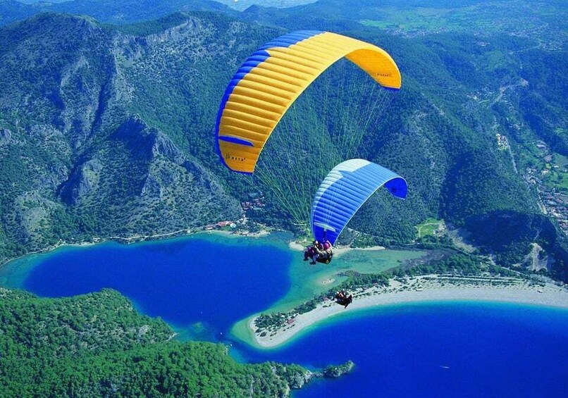 Two paragliders flying over a coastal area with lush green mountains and a large body of water. 1