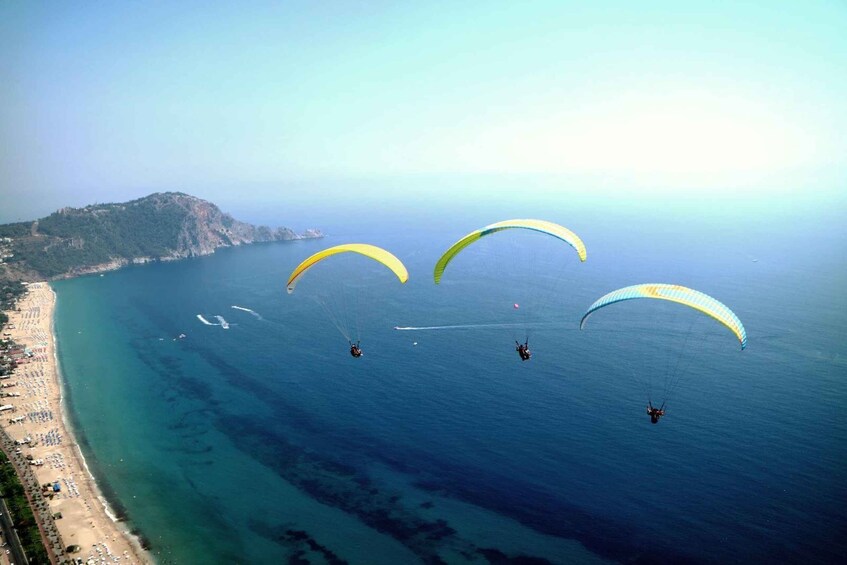 A coastal area with a beach and cliffs. There are several paragliders in the air. 5