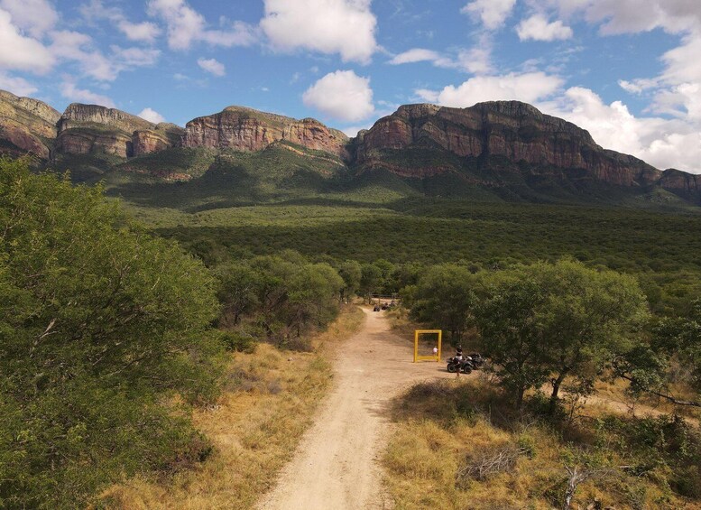 A dirt path leading through a green landscape with mountains in the background. 3