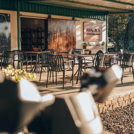 An outdoor seating area with wooden tables and chairs, a sign reading 'MY AFRICA ADVENTURE FARM,' and a covered entrance. 1