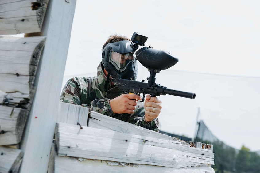 A person in camouflage gear aiming a paintball gun at a target. 1