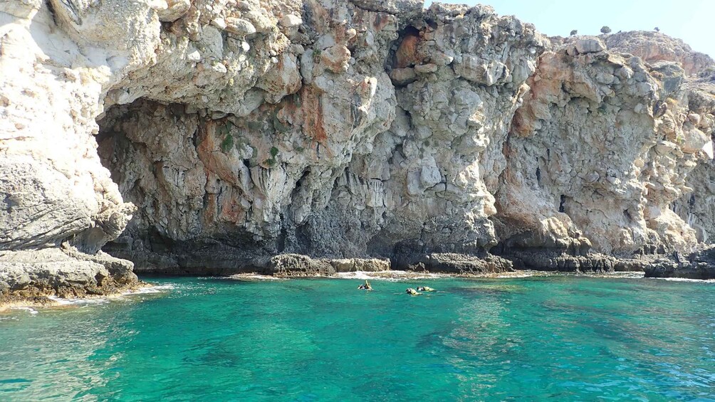 A rocky coastline with clear turquoise water and people swimming. 2