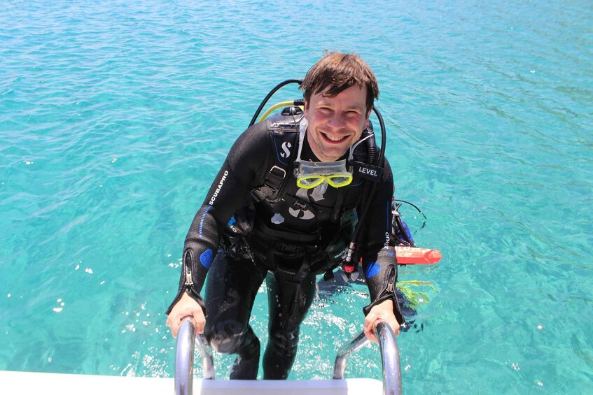 A person in a black wetsuit with scuba gear, standing in clear blue water. 3