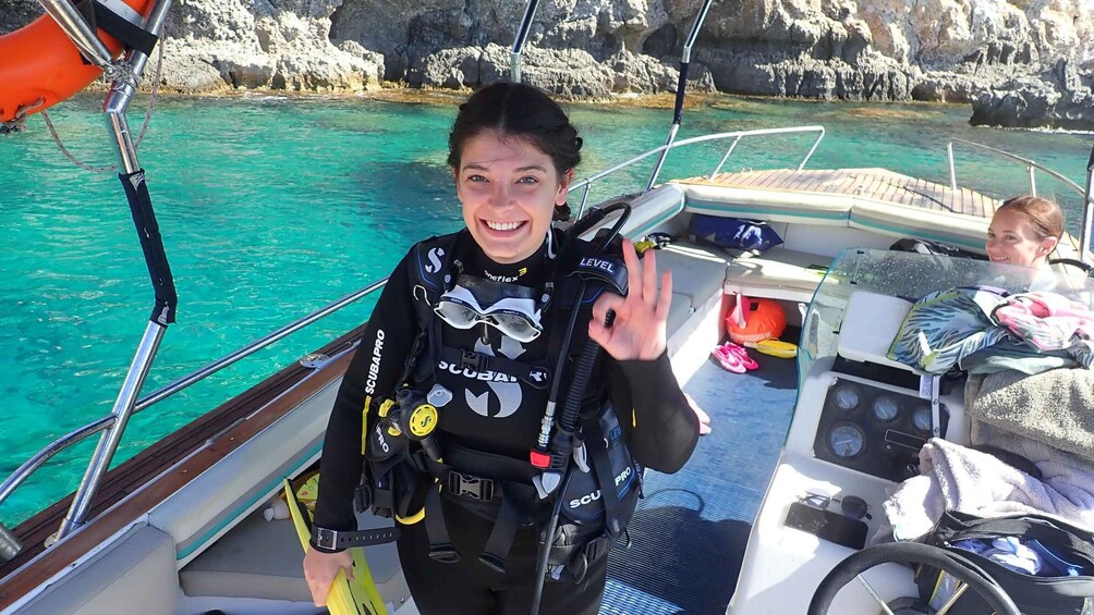 A diver on a boat with clear turquoise water and rocky cliffs in the background. 1