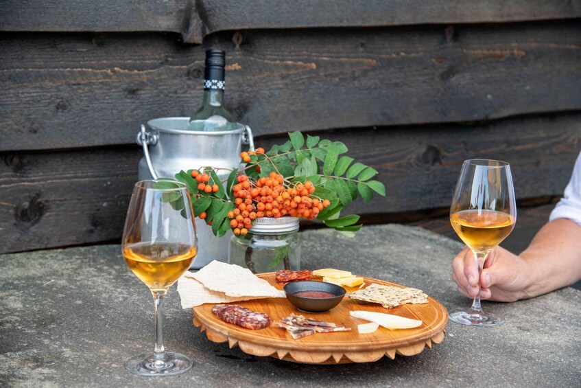 A wooden tray with cheese, charcuterie, and a bottle of wine, with a rustic backdrop. 4