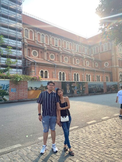 A couple standing in front of a historic building with arched windows and a brick facade. 1