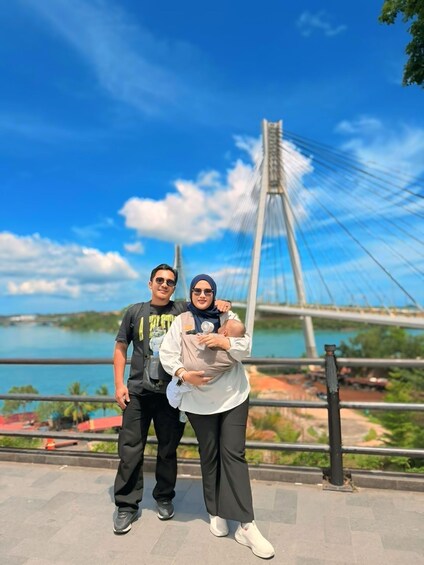 A couple with a baby, a bridge, and a body of water in the background. 2