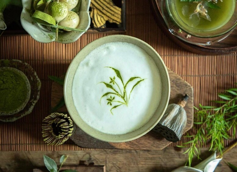 A bowl of white liquid with a green garnish, surrounded by various bowls and a spoon on a wooden surface. 5