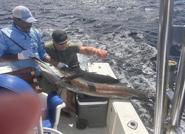 Two people on a boat holding a large fish. 5