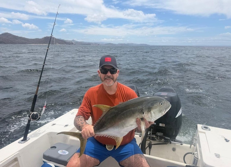 A man in a boat holding a fish, with a fishing rod and calm sea in the background. 1