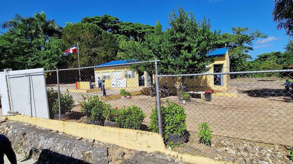 A fenced area with a building, a flag, and greenery. 5