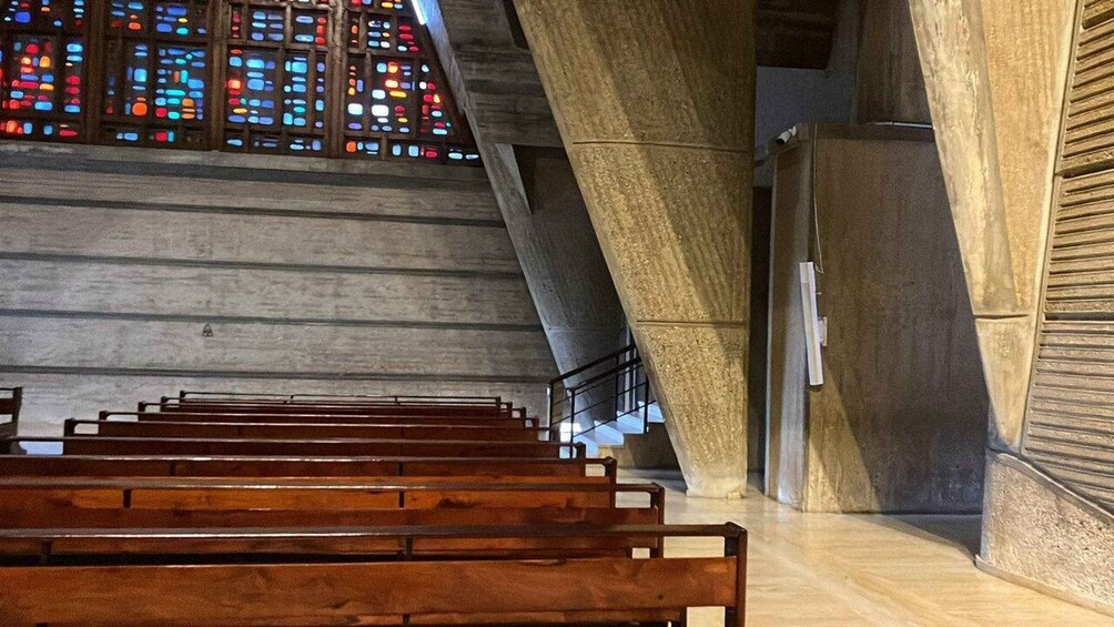 A church interior with wooden pews, stained glass windows, and a concrete structure. 3