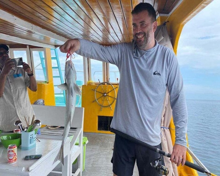 A person holding a fish on a boat with a steering wheel and a table with a can of drink and utensils. 5