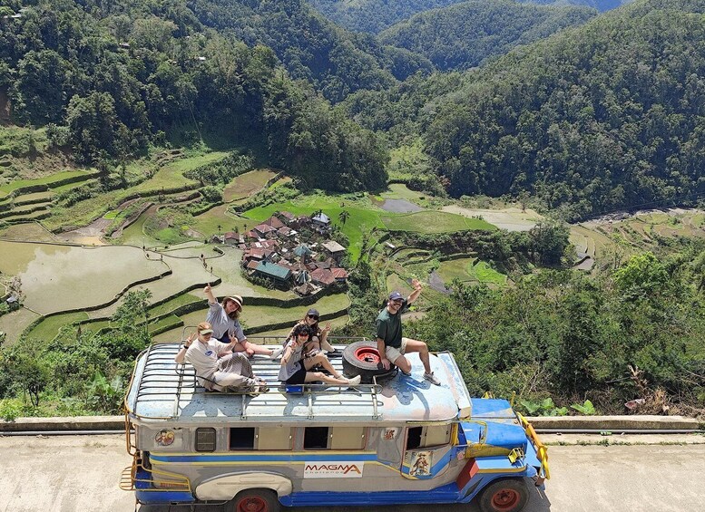 A group of people on a colorful bus with a scenic view of terraced fields and a small village in the background. 3