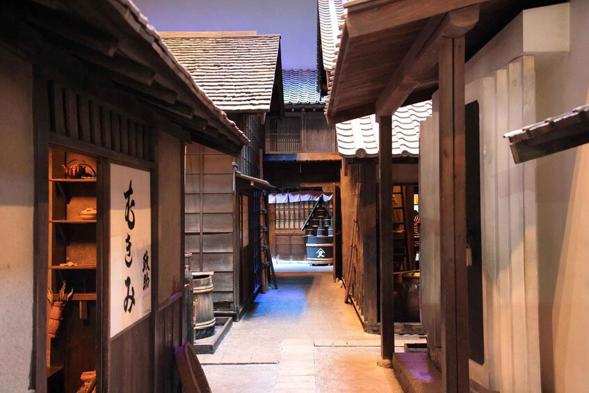 A narrow alleyway with traditional wooden buildings, some with signs in a foreign script, and a clear sky above. 1
