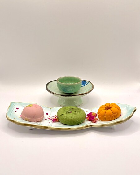 A ceramic tray with three colorful, textured objects and a green bowl. 2