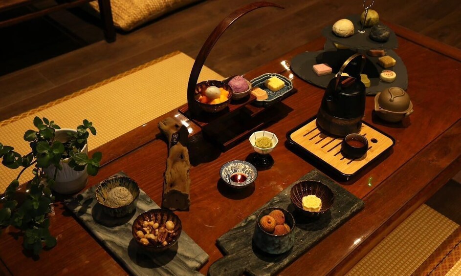 A traditional Japanese tea ceremony setup with a wooden table, tea utensils, and various sweets. 1