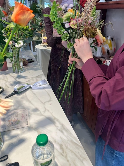 A person arranging flowers on a table with a vase, scissors, and a bottle of water. 3