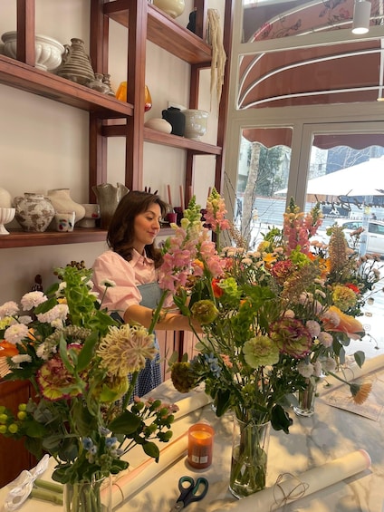 A person arranging flowers in a shop with shelves of pottery and a window view. 1