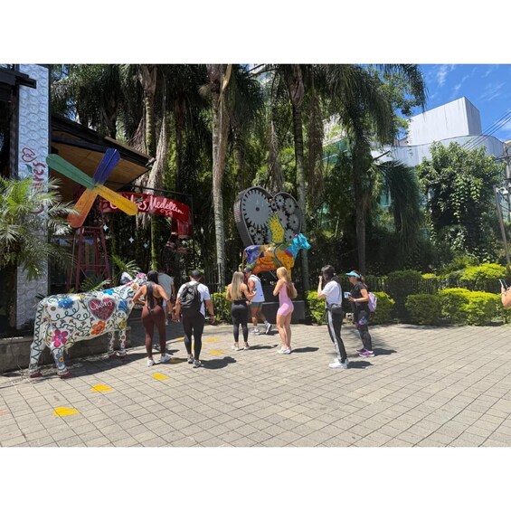 A colorful street scene with a decorative cow statue, a clock, and people walking. 3