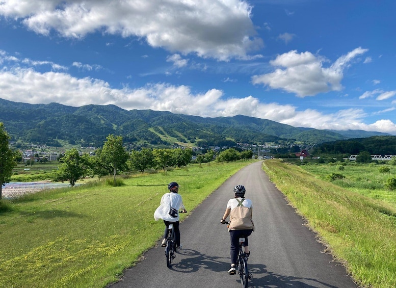 Two cyclists on a rural road with mountains in the background. 2