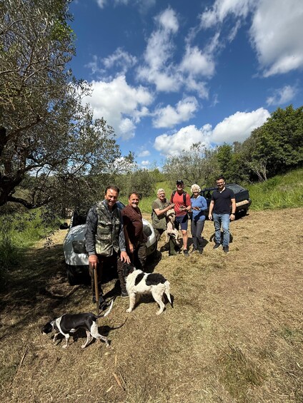 A group of people with a dog in a grassy field with trees and a clear sky. 3