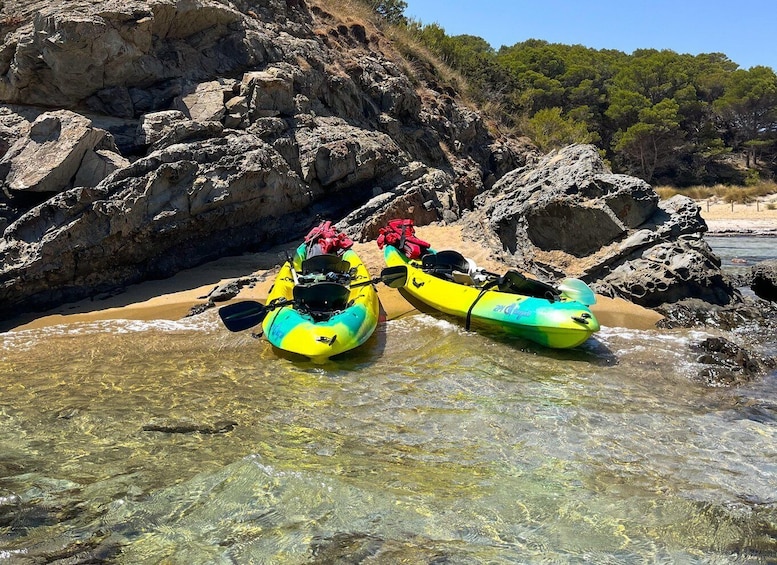 Two yellow and green kayaks on a rocky beach with clear water. 2