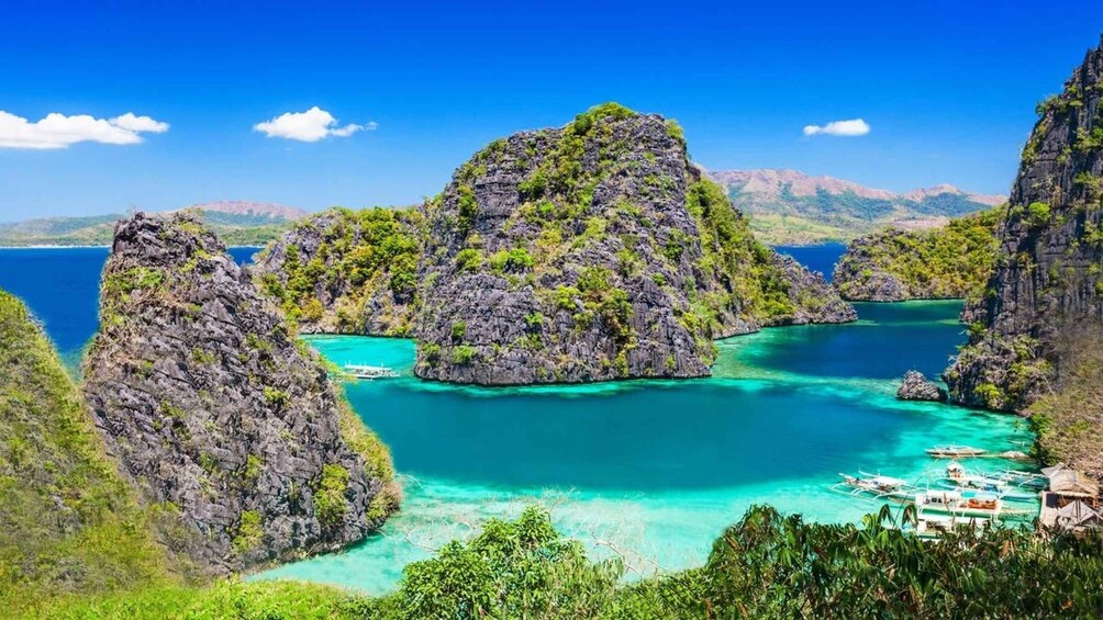 A coastal landscape with rocky formations, clear turquoise waters, and boats anchored near the shore. 3