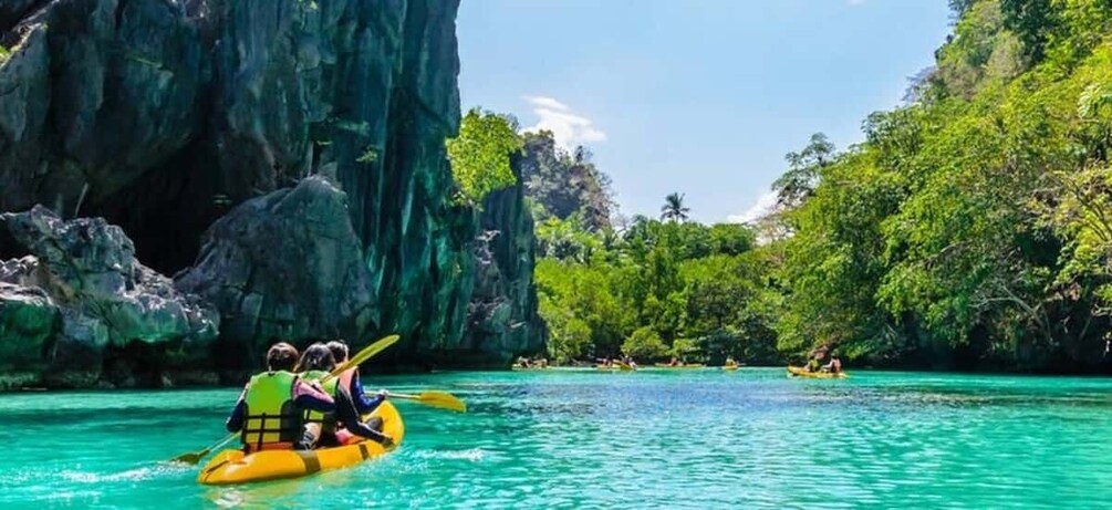 A group kayaking on turquoise water with a rocky cliff and lush greenery in the background. 5