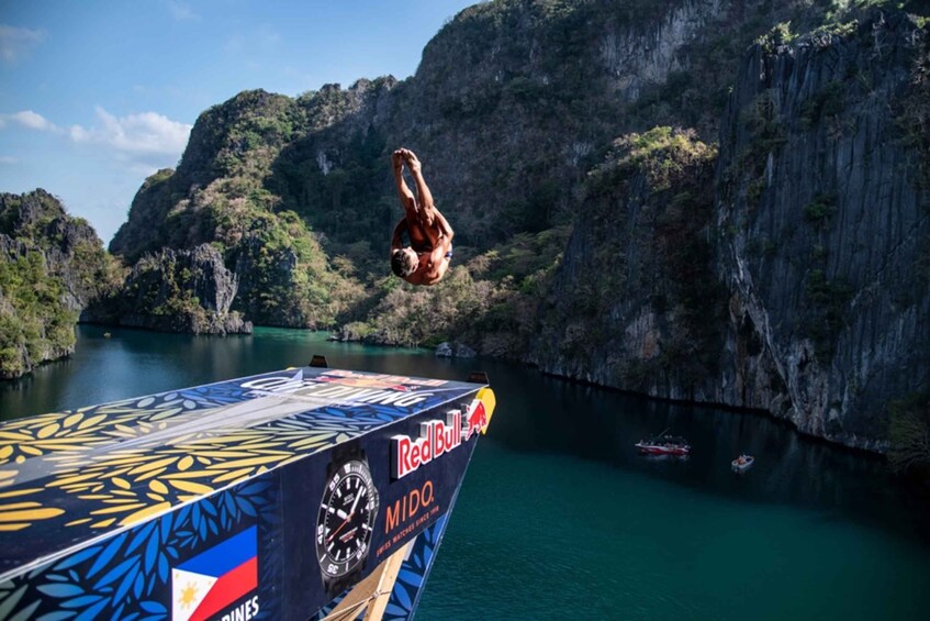 A person mid-air performing a dive from a Red Bull diving platform into a body of water surrounded by cliffs. 2