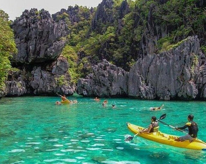 People kayaking in clear turquoise water surrounded by rocky cliffs and lush greenery. 4