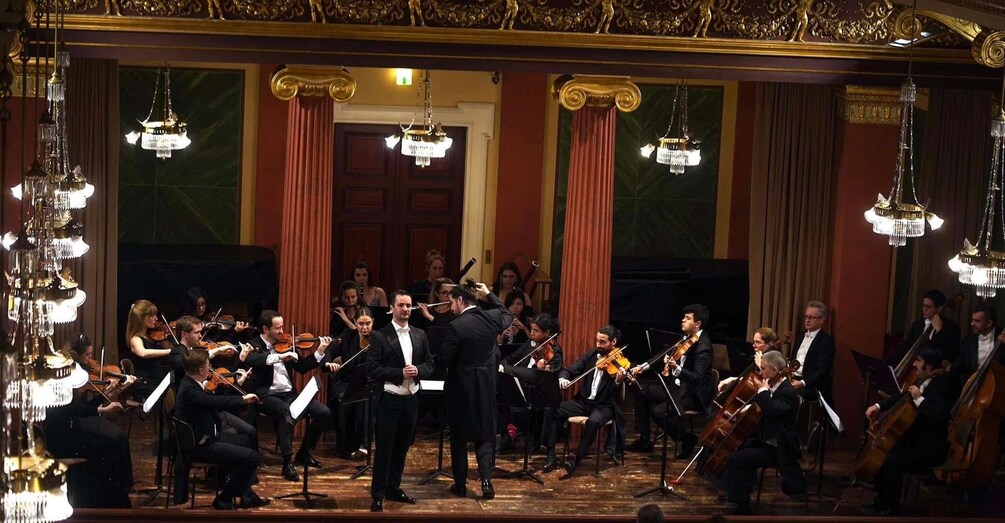 A classical orchestra performing in a grand hall with ornate chandeliers and columns. 4