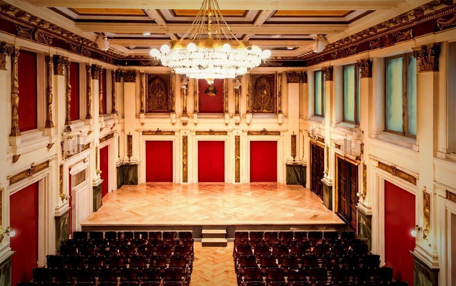 A grand hall with ornate columns, a large chandelier, and rows of chairs. 1