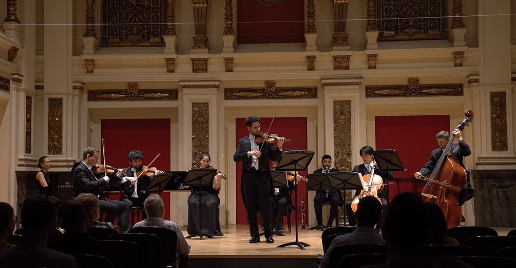 A classical music concert with musicians on stage and an audience seated in front. 3