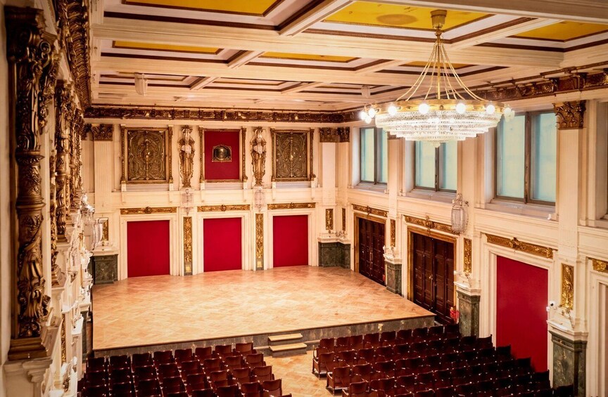 An ornate theater with a stage, rows of red seats, and elaborate ceiling decorations. 2