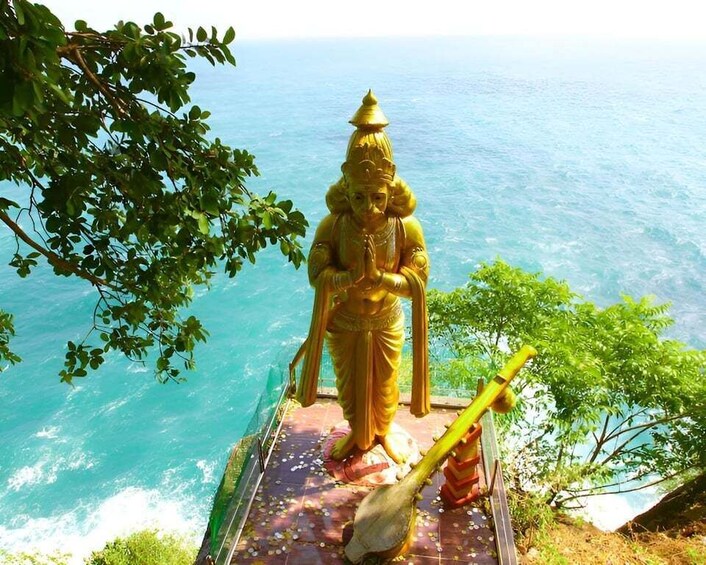 A golden statue of a deity with a drum, set against a coastal backdrop. 5